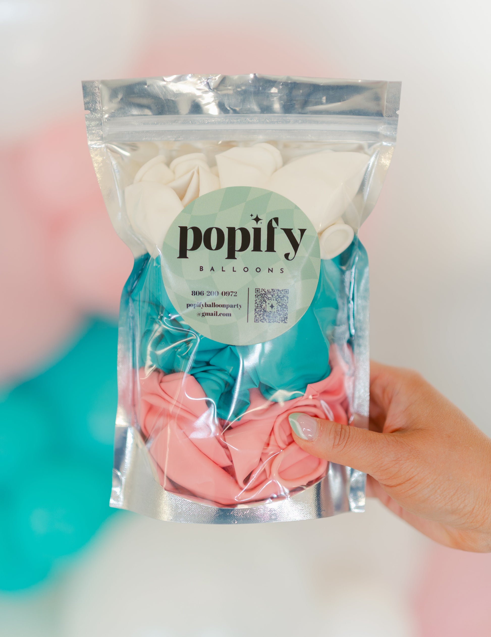 Packaged pink balloons with 'popify' label held by a hand against a blurred background