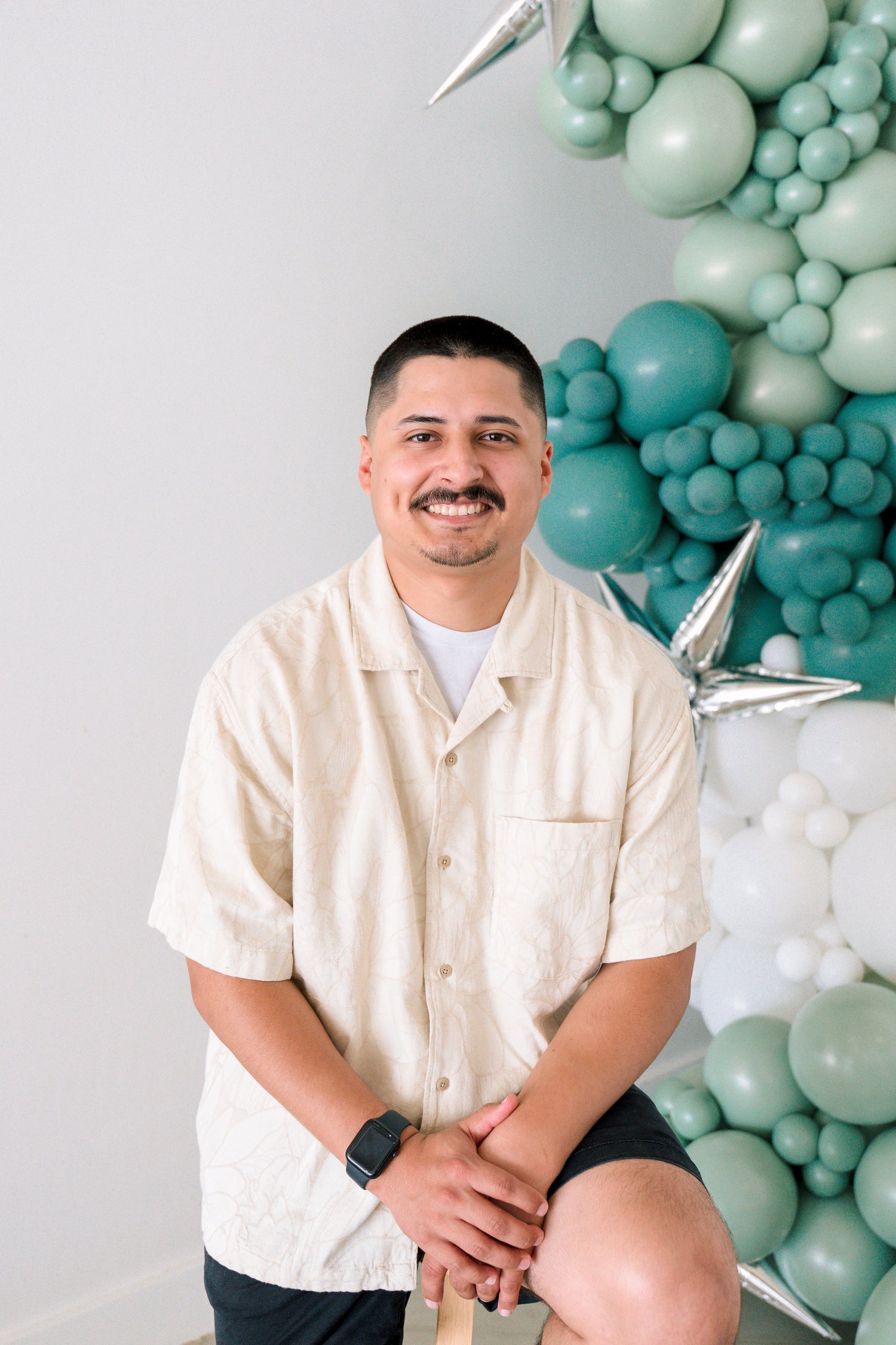 Man posing in front of a teal balloon arch